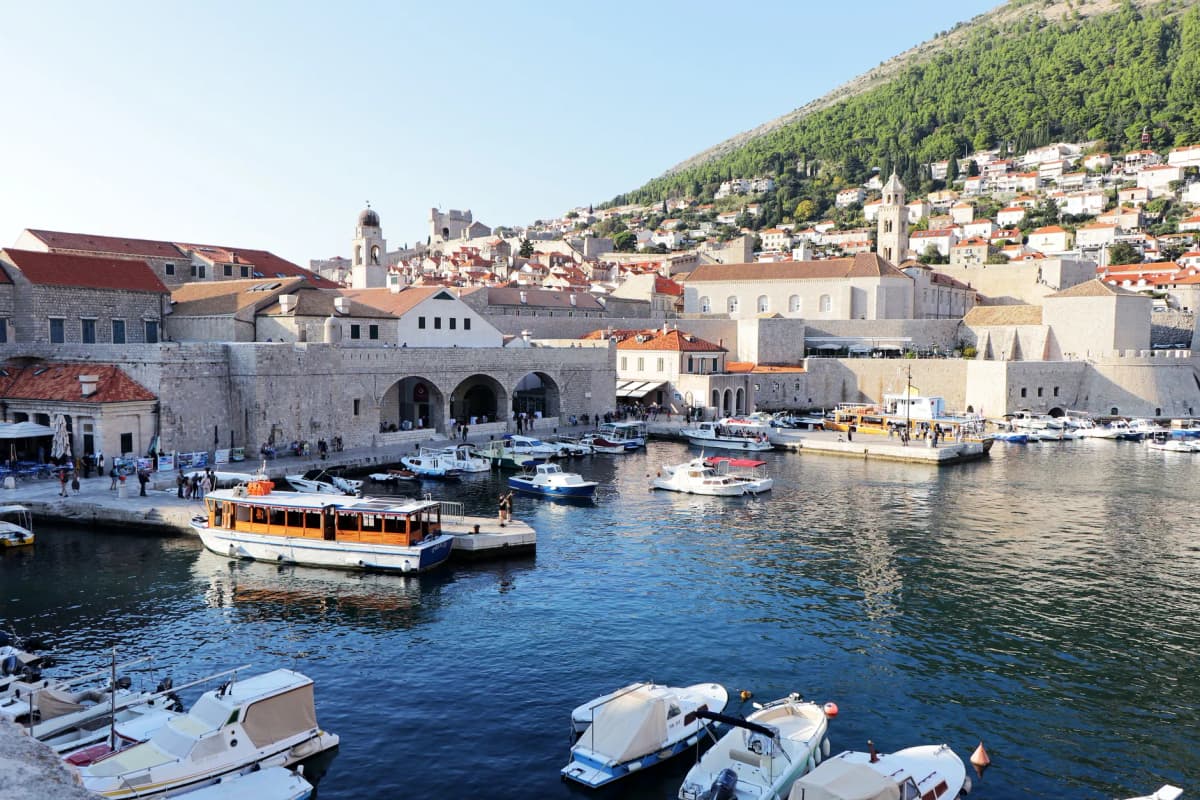 Explore the stunning Dubrovnik harbor with boats and historic architecture under a sunny sky.