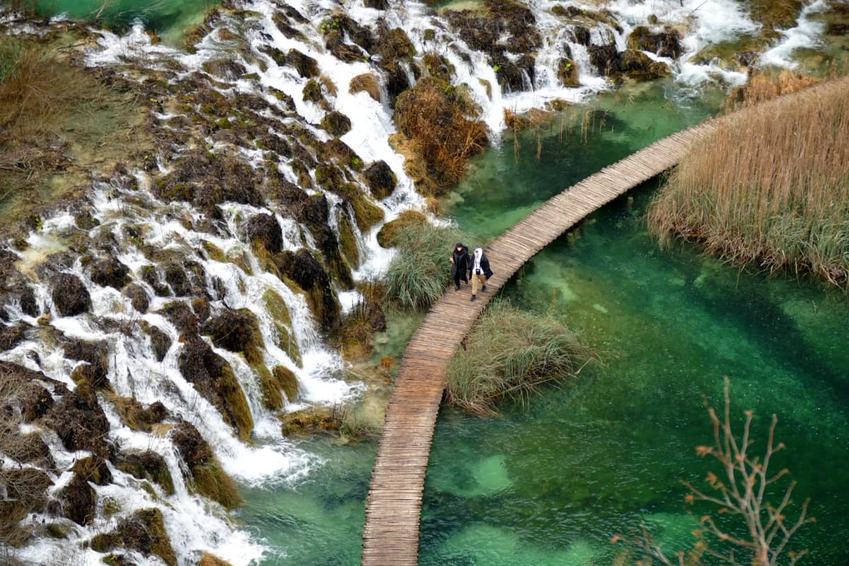 A breathtaking aerial view of Plitvice Lakes in Croatia with a couple walking on a scenic wooden path.